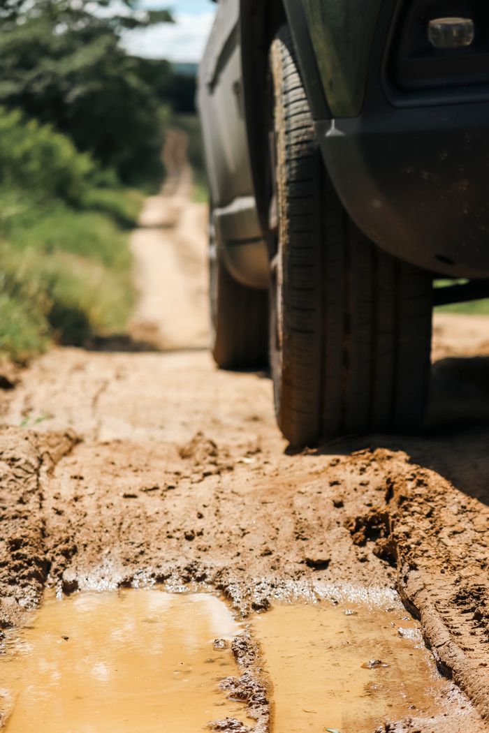 A rugged vehicle navigates a challenging muddy dirt road through scenic outdoor terrain.