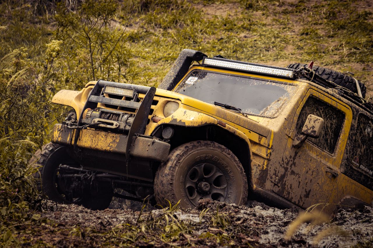 Yellow 4x4 SUV tackling a muddy off-road path in a rugged outdoor setting.