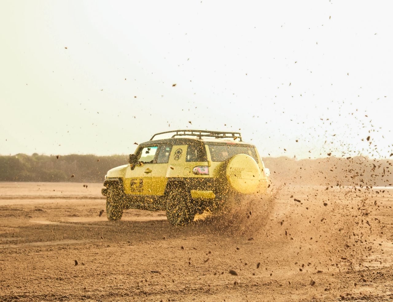 Yellow SUV creating a dramatic display of dust while driving off-road in a desert setting.